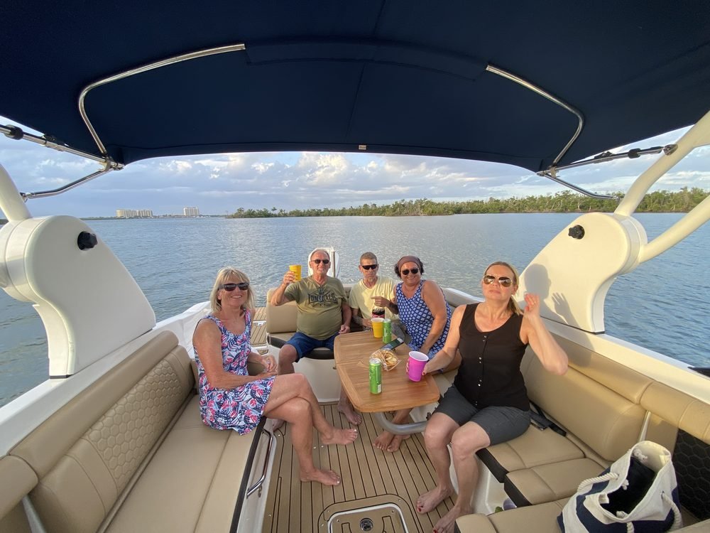 A group of guests relaxing with drinks and snacks aboard a private boat tour at golden hour, Cape Coral skyline in the distance