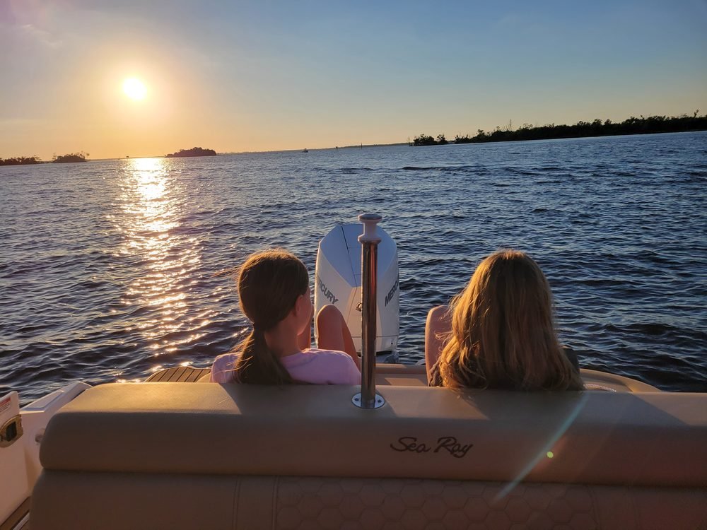 Two kids seated at the stern of the Sea Ray boat watching the sunset over the water